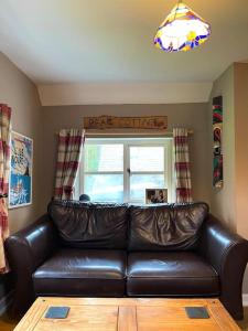 un canapé en cuir dans un salon avec une fenêtre dans l'établissement Bear Cottage, Tyn Y Cwm, à Scyborycoed