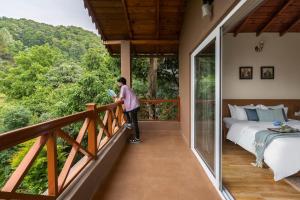 a person standing on the balcony of a house at SaffronStays Plaksha - 2BR pet-friendly homestay with Himalayan views, verandah dining & bonfire near Chauli ki Jali in Mukteshwar