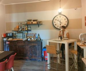 a woman sitting at a table with a clock on the wall at B&B CountryHouseAnna in Crema