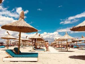 una playa con muchas sombrillas de paja y gente en ella en Studio Alezzi Beach Resort Ely en Năvodari