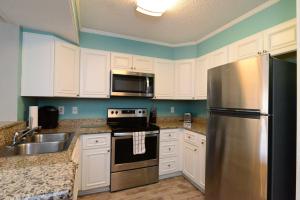 a kitchen with white cabinets and a stainless steel refrigerator at Sweet Caroline Remodeled with Partial Ocean View and Oceanfront Pool in Myrtle Beach