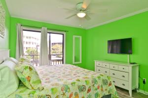 a green bedroom with a bed and a flat screen tv at Sweet Caroline Remodeled with Partial Ocean View and Oceanfront Pool in Myrtle Beach