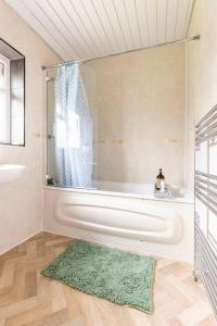 ein Badezimmer mit einer Badewanne, einer Dusche und einem Teppich in der Unterkunft Spacious 3-Bed House with car park near Heathrow in Hounslow