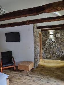 a room with a stone wall and a chair and a tv at Rooms Villa Ruja in Grabovac
