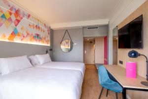 um quarto de hotel com uma cama branca, uma secretária e uma televisão em Allegro Agadir em Agadir