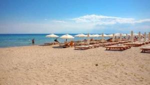 a beach with tables and umbrellas and the ocean at Studio Coral by the sea in Neoi Epivates