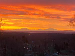 una puesta de sol con montañas en el fondo y una ciudad en Alaskan Adventure Awaits!, en Eagle River