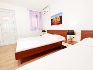 two beds in a room with white walls and wooden floors at Apartmani Buljubašić in Baška Voda