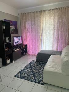 a bedroom with a bed and a tv and pink curtains at Apt no Melhor local em Lauro de Freitas in Lauro de Freitas