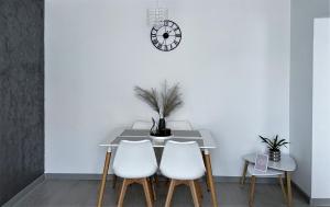 a dining room table with three white chairs and a clock at Inga Apartment in Turda