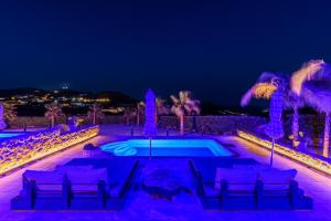 una piscina notturna con sedie e palme di Aurora Mykonos Villas a Kalafatis