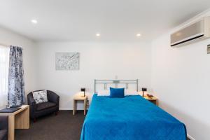 a bedroom with a blue bed and a chair at Camelot Motor Lodge and Conference Centre in Palmerston North