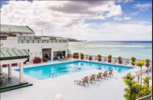 a pool with chairs and the ocean in the background at Alupang Beach Tower, UPGRADED units in Tamuning