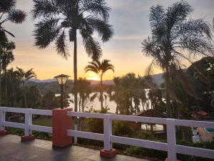 a sunset over the water with palm trees and a fence at Pousada Solar das Palmeiras in Joanópolis