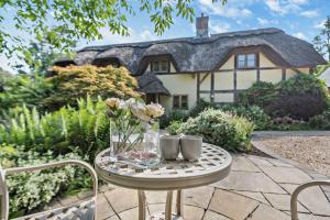 a table with a vase of flowers and two mugs at The Cottage, Beautiful New Forest 5 Bedroom Thatched Cottage in Breamore