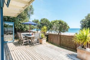a wooden deck with a table and umbrella and the beach at Onetangi Waterfront Bach - Coast & Country in Onetangi