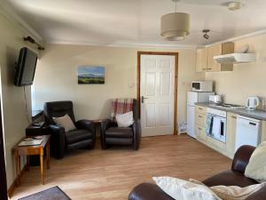 a living room with two chairs and a kitchen at Corehouse Farm Cottages - Dairy, Granary & Sawmill in Lanark