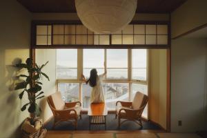 Eine Frau, die aus dem Fenster eines Gebäudes schaut. in der Unterkunft Hotel 2YL Atami in Atami