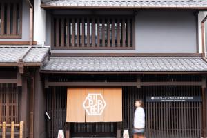Ein Mann geht mit einem Schild an einem Gebäude vorbei. in der Unterkunft Mitsui Garden Hotel Kyoto Shinmachi Bettei in Kyoto