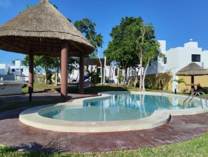 una gran piscina con sombrilla de paja y césped en Casa en privada con alberca, Excelente para vacaciones y descanso, en Playa del Carmen