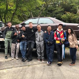 a group of people standing in front of a car at YUMORI ONSEN HOSTEL in Fukushima