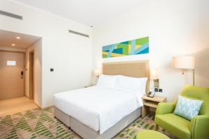 a bedroom with a white bed and two green chairs at Holiday Inn & Suites - Dubai Science Park, an IHG Hotel in Dubai