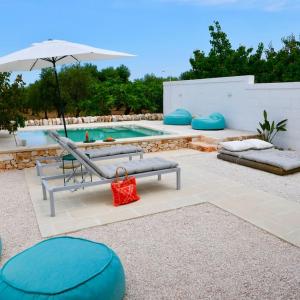 a pool with a bench and an umbrella and a red bag at Masseria Pezze Galere-La Casa del Fico con piscina idromassaggio privata in Fasano