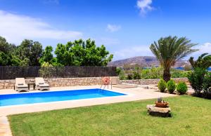 une piscine dans un jardin avec une pelouse et des arbres dans l'établissement Muses Beach Villas - Cleo, à Siteía