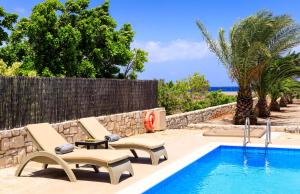 une piscine avec deux chaises longues à côté d'une clôture dans l'établissement Muses Beach Villas - Cleo, à Siteía