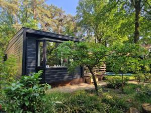 una pequeña casa negra en el bosque en Heerlijk Huisje in het bos op Chaletpark Kempenbos en Diessen
