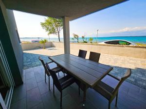 een houten tafel en stoelen op een patio met uitzicht op het strand bij Apartmani Adria in Nin
