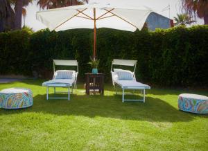 three chairs and an umbrella in the grass at Villa Incanto on the Sea in Siracusa