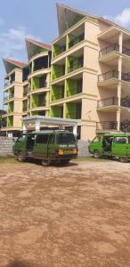 dwa zielone furgonetki zaparkowane przed budynkiem w obiekcie Sky Beach Hotel w mieście Wakiso