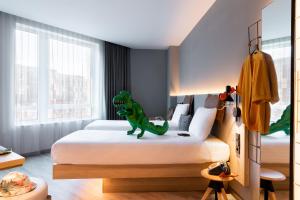 un jouet de dinosaure assis sur un lit dans une chambre dans l'établissement Moxy The Hague, à La Haye