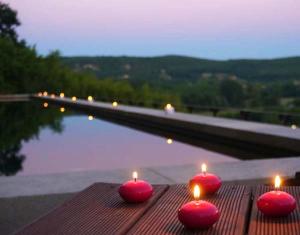 3 bougies rouges assises sur une table à côté d'une piscine dans l'établissement Sarrasins Bed and Breakfast, à Beynac-et-Cazenac