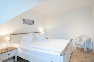 a white bedroom with a bed and a chair at Lieblingsort Dankbarkeit in Timmendorfer Strand