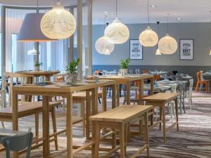 restauracja z drewnianymi stołami, krzesłami i światłami w obiekcie Novotel Kraków City West w Krakowie