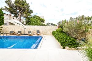 a pool with chairs and an umbrella next to a wall at Villa Cornea - Luxury Villa in a heart of Novalja in Novalja