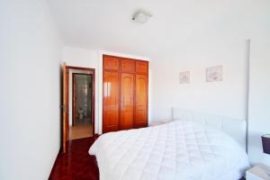 a white bedroom with a white bed and a wooden door at Amazing Apartments in Agualva