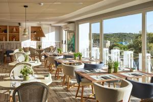 un restaurante con mesas, sillas y ventanas grandes en Catalonia Mirador des Port en Mahón