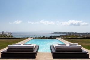 a swimming pool with two lounge chairs next to the ocean at Villa Ainar in Tinos Town