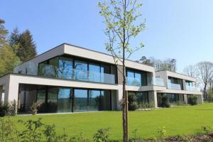 une maison avec de grandes fenêtres et une pelouse verte dans l'établissement Au bois du Sart-Tilman, à Sur le Mont