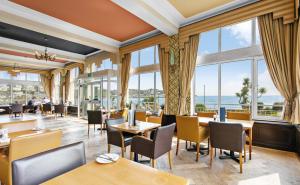 un restaurante con mesas, sillas y ventanas grandes en The Grand Hotel en Torquay