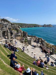 a group of people sitting on the grass near the water at The Old Workshop - Drift in Penzance