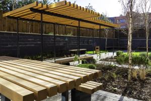 eine Holzbank in einem Garten mit einem Pavillon in der Unterkunft For Students Only - The Valentine in London in Ilford