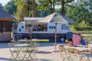 un camión de comida con gente sentada en mesas y un paraguas en Huttopia De Meinweg, en Herkenbosch
