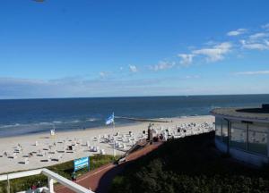 - une plage avec des chaises blanches, un bâtiment et l'océan dans l'établissement WoogeBella - Traumblick auf die Nordsee, à Wangerooge