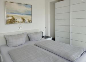 ヴァンガーオーゲにあるWoogeQueen - 112 m² Luxus mit direktem Meerblickの白いベッドルーム(ベッド1台付)が備わります。壁には絵画が飾られています。
