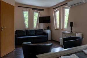 sala de estar con sofá negro y ventanas en Accomo Apartmanház en Siófok