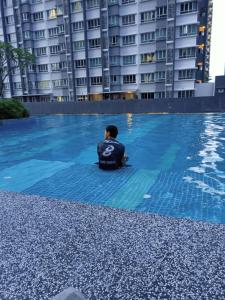 un hombre sentado en el agua en una piscina en KL Homestay@Savanna Executive Suite, en Bangi